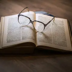 Eine Brille liegt auf einem aufgeschlagenen Buch mit informierenden Texten.