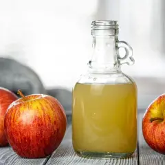Aceto di mele in bottiglia con mele rosse. Un rimedio naturale per la gastrite nervosa, semplice e salutare.