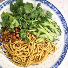 En läcker asiatisk nudelsallad med krispig gurka, rostade jordnötter och färsk koriander på en vackert mönstrad tallrik.