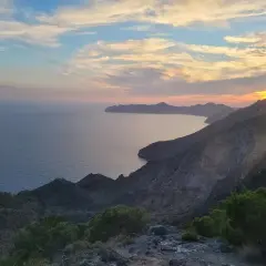 Atardecer en el mirador del Roldán, con el mar Mediterráneo y montañas escarpadas bajo un cielo de nubes rosadas y anaranjadas.