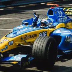Un coche de Renault F1 azul y amarillo, con el piloto saludando.