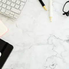 Na biurku leżą klawiatura, notatnik, telefon, długopisy i okulary. To miejsce pracy, gdzie można znaleźć informację o warunkach zatrudnienia.