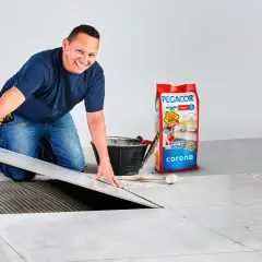 Instalador coloca baldosa sobre adhesivo. Bolsa de Pegacor y herramientas, para saber como se calcula la superficie.