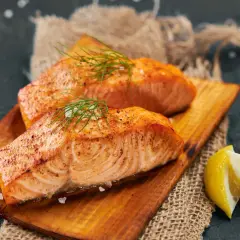 Deux pavés de saumon grillé, parsemés d'aneth et de gros sel, servis sur une planche en bois avec des quartiers de citron. Un délice pour accompagner un bon vin.