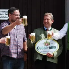 Vier Männer stoßen mit Biergläsern an. Einer hält ein Schild der Osser Brauerei.