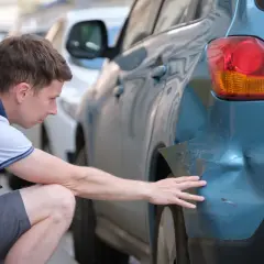 Mann untersucht Delle am blauen Auto. Hoffentlich keine Geisterfahrer-Strafe wegen des Schadens.