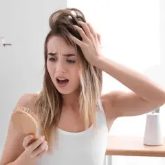 Mujer preocupada por la caida de pelo en verano, con mechones en el cepillo.
