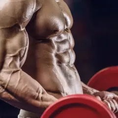 Ein Mann mit stark definierten Bauchmuskeln und Armen hebt eine Hantel. Die Muskelpumpe ist deutlich sichtbar, ein Zeichen intensiven Trainings.