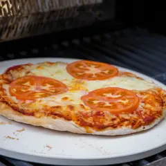 Eine Margherita-Pizza mit Tomatenscheiben und geschmolzenem Käse wird auf einem Pizzastein im Backofen gebacken.