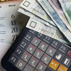 Kalkulator fiskalny z polskimi banknotami. Obok kalendarz z datami. Możliwe, że to przygotowanie do rozliczenia kwoty zmniejszającej podatek.