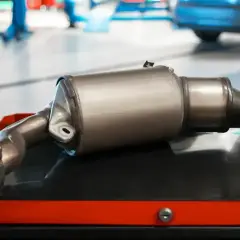 Nowy katalizator samochodowy, czyli GPF (Gasoline Particulate Filter), leży na wózku warsztatowym.