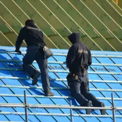Dwaj dekarze układają membranę dachową, kluczowy element ochrony domu przed wilgocią.