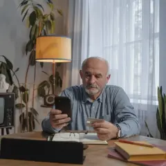 Starszy pan sprawdza w telefonie, ile kosztuje przedłużenie w lombardzie.