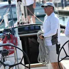 Equipaggio barca a vela pronto per la regata. Un uomo tiene una cima, una donna è seduta, mentre un altro uomo è al timone.