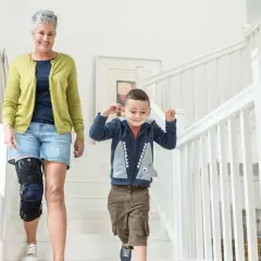 Frau mit Kniebandage, die mit ihrem Enkel die Treppe hinuntergeht. Einlagen bei Kniearthrose können helfen, die Mobilität zu verbessern.