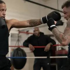 Two boxers spar in a ring, one throwing a jab, demonstrating how to counter punch. A coach watches from the background.