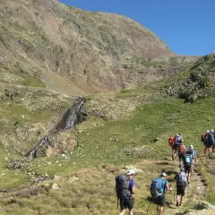 Senderistas caminan por un sendero de montaña hacia una cascada, como si fuera la porta del cel.