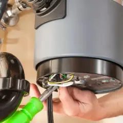 A person is working on a garbage disposal that is not working, connecting wires with a screwdriver.