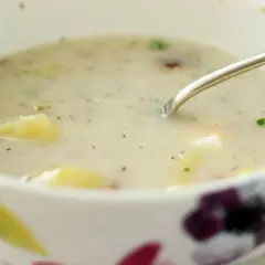 Aksamitny barszcz biały z ziemniakami, doprawiony ziołami, w misce z kwiatowym wzorem. Łyżka zanurzona w zupie.