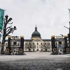 Grön flagga med texten "Armémuseum" vid krigsmuseum Stockholm. Imponerande byggnad med kupol och staket.