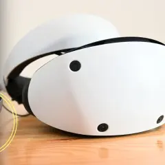 Zwei weiße PSVR 2 Headsets liegen auf einem Holztisch. Ein gelbes Fragezeichen symbolisiert die Ungewissheit.