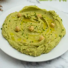 Hummus de aguacate cremoso, decorado con garbanzos, aceite de oliva, semillas de sésamo y cebollino. ¡Un entrante delicioso!