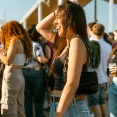 Uśmiechnięta dziewczyna cieszy się atmosferą jednego z letnich festiwali muzycznych. Wokół tłum ludzi, słońce i dobra zabawa.
