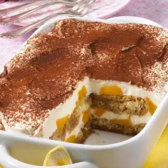 Ein cremiges Pfirsich Tiramisu, bestäubt mit Kakao, in einer weißen Auflaufform. Saftige Pfirsichstücke und Löffelbiskuits sind geschichtet.