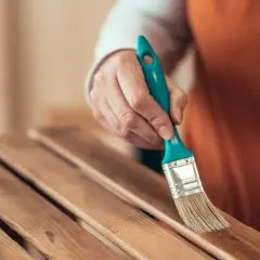Mano con brocha lijando listones de madera barnizada para restaurar un mueble.