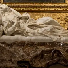Śpiąca postać z marmuru, dzieło słynnych rzeźbiarzy i ich dzieła, spoczywa na bogato zdobionym postumencie.