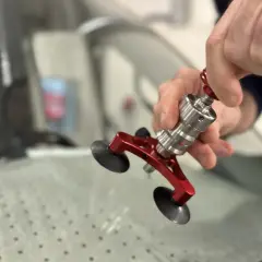 En person använder ett verktyg för att laga en spricka i en bilruta. Verktyget har sugproppar och en metallkonstruktion.