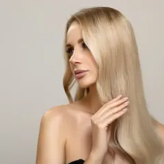 Kobieta z pięknymi, długimi włosami w odcieniu brzoskwiniowy blond, delikatnie dotyka ich dłonią.