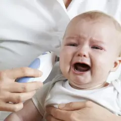 Płaczące dziecko z termometrem w uchu. Prawdopodobnie zapalenie ucha u dziecka.