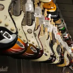 Rząd gitar elektrycznych w sklepie. Widać różne kolory i modele, w tym pierwsza gitara elektryczna z pięknym wykończeniem.
