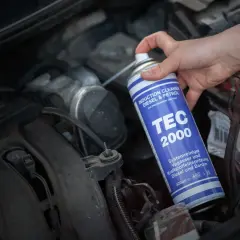 Ręka trzyma puszkę TEC 2000, wykonując czyszczenie kolektora dolotowego silnika.