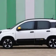 Biały fiat pandina z żółtymi lusterkami stoi na tle zielono-białej ściany.