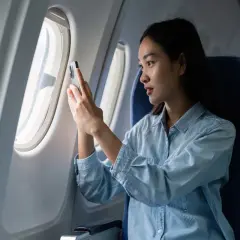 Kobieta w samolocie sprawdza telefon, zastanawiając się, czy w samolocie jest internet.