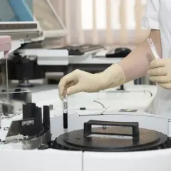 Ręka w rękawiczce umieszcza probówkę z ciemnym płynem w aparacie laboratoryjnym. To co to za badanie?