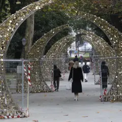 Personas pasean bajo arcos dorados decorados con luces, preparándose para el encendido de luces en Oviedo.