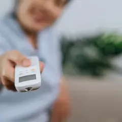 Persona sonriente ajusta el aire acondicionado con el mando. Controla la potencia aire acondicionado kw para un confort ideal.