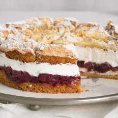 Eine köstliche Hansen Jensen Torte mit Kirschen, Sahne und Baiserhaube, bestreut mit Mandelblättchen und Puderzucker.