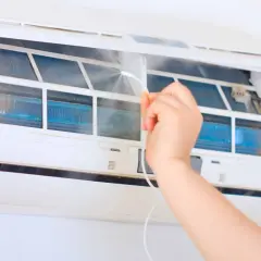 Czyszczenie klimatyzacji w domu. Ręka spryskuje wnętrze urządzenia, dbając o odgrzybianie i świeże powietrze.