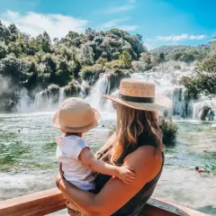 Mama z dzieckiem podziwia piękne krka wodospady. Woda w rzece jest krystalicznie czysta, a wokół bujna zieleń.