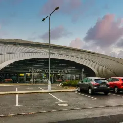 Nowoczesne lotnisko w Czechach, Karlowe Wary, z charakterystyczną, falistą fasadą. Dwa samochody stoją na parkingu przed wejściem.