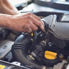 Ręce mechanika pracujące przy silniku samochodu, widoczne przewody i żółta zakrętka.