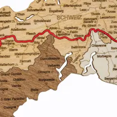 Drewniana mapa Alp z zaznaczoną trasą Via Alpina, pokazująca szczyty i miejscowości takie jak Matterhorn, Zermatt, Lugano i St. Moritz.