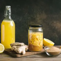 Zutaten für ingwer fermentieren: frischer Ingwer, Zitronen, Orangen und Zucker. Daneben eine Flasche mit gelbem Getränk.