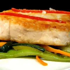 Bonito jugoso sobre verduras salteadas, con tiras de pimiento rojo.