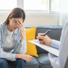Kobieta z ręką na czole siedzi na kanapie, rozmawiając z terapeutą. Może to być rozmowa o diagnozie Aspergera.