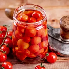 Glas voller Tomaten, bereit zum Einkochen wie Oma. Frische Kirschtomaten und ein Einkochgerät auf Holzuntergrund.